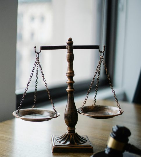 Decorative judgement scale and gavel placed on desk in light lawyer office against window